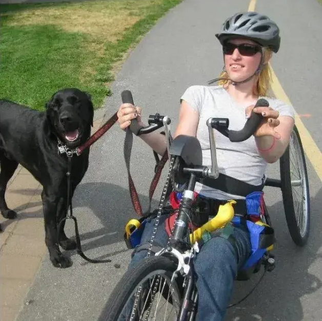 Woman on a hand cycle with her dog on a sunny path